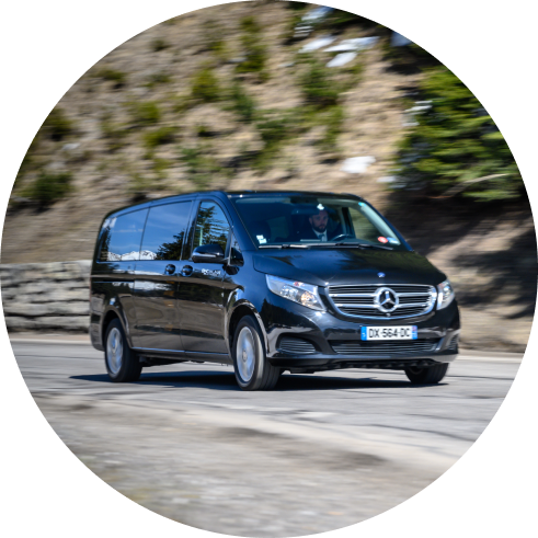 A black Mercedes-Benz van moving swiftly on a road with blurred trees in the background.