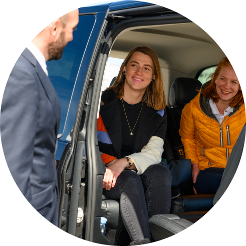 Two smiling young women, one in a black jacket and one in a yellow jacket, seated in the back of a vehicle.